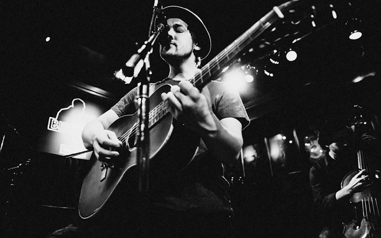 black and white photo of jon kenzie on a live show singing and playing guitar
